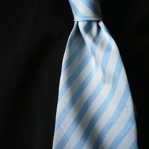 May include: A light blue and white striped tie against a black backdrop. The tie is knotted, with the stripes running vertically down the fabric. The fabric has a slight sheen.