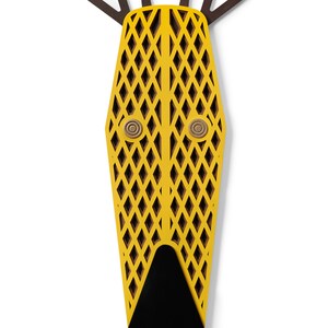 K&ouml;nnte beinhalten: Eine gelbe Holzmaske mit geometrischem Muster und schwarzen Augen. Die Maske hat eine schwarze Nase und drei braune H&ouml;rner oben.