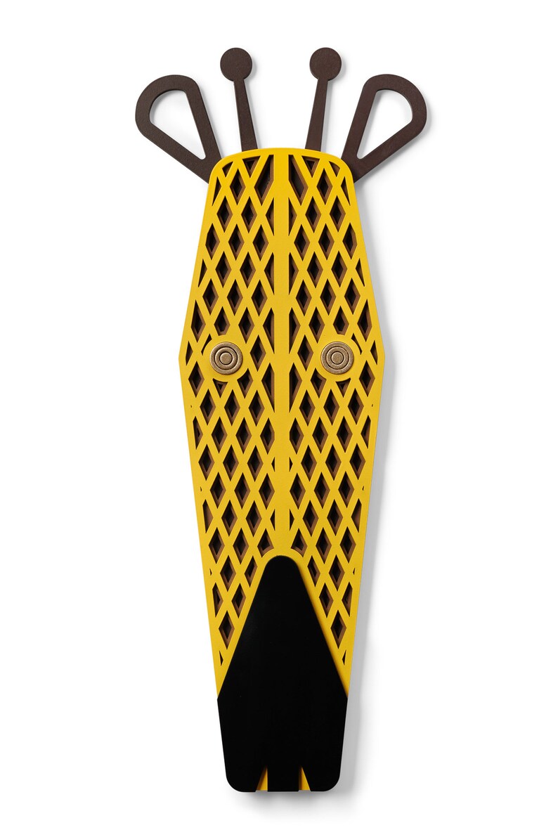 K&ouml;nnte beinhalten: Eine gelbe Holzmaske mit geometrischem Muster und schwarzen Augen. Die Maske hat eine schwarze Nase und drei braune H&ouml;rner oben.
