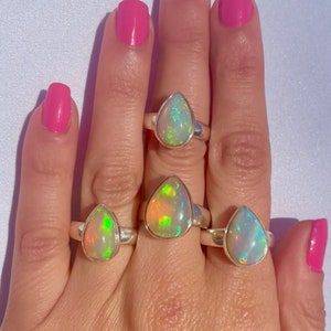 Puede incluir: Tres anillos de plata con piedras preciosas de &oacute;palo en forma de l&aacute;grima. Los &oacute;palos son iridiscentes con tonos de verde, amarillo y blanco.