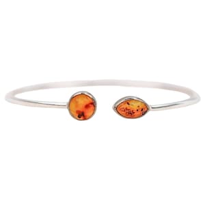 May include: A silver open cuff bracelet with two amber stones. One stone is round, the other is oval. The bracelet is displayed against a white background, emphasizing the jewellery's design and materials.