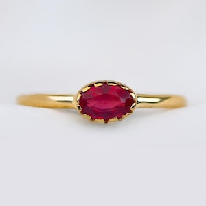 May include: A gold ring with a red oval gemstone set in a delicate, scalloped bezel.