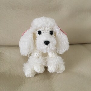 Peut inclure: Jouet en crochet de caniche blanc avec des oreilles roses. Le jouet est assis sur un canap&eacute; brun clair.
