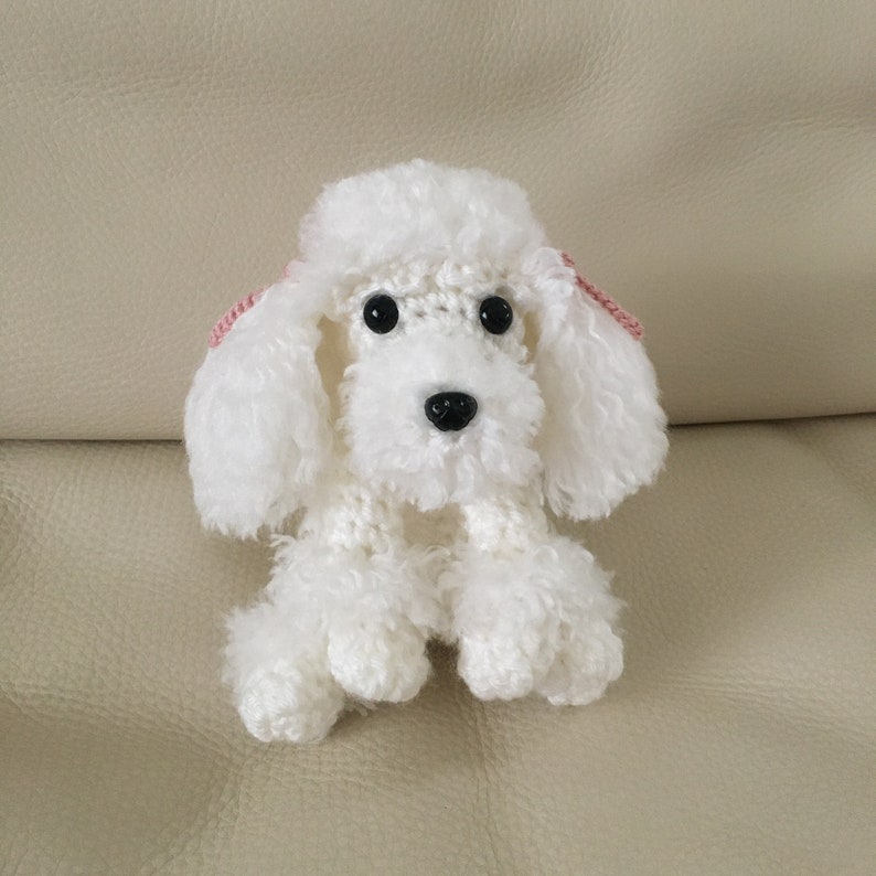 Peut inclure: Jouet en crochet de caniche blanc avec des oreilles roses. Le jouet est assis sur un canap&eacute; brun clair.