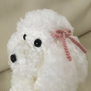 Peut inclure: Poodle blanc en crochet avec des yeux noirs et un n&oelig;ud rose.