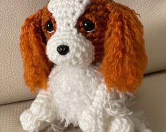 May include: A crocheted stuffed toy dog with white fur and brown ears. The dog has black eyes and a black nose.