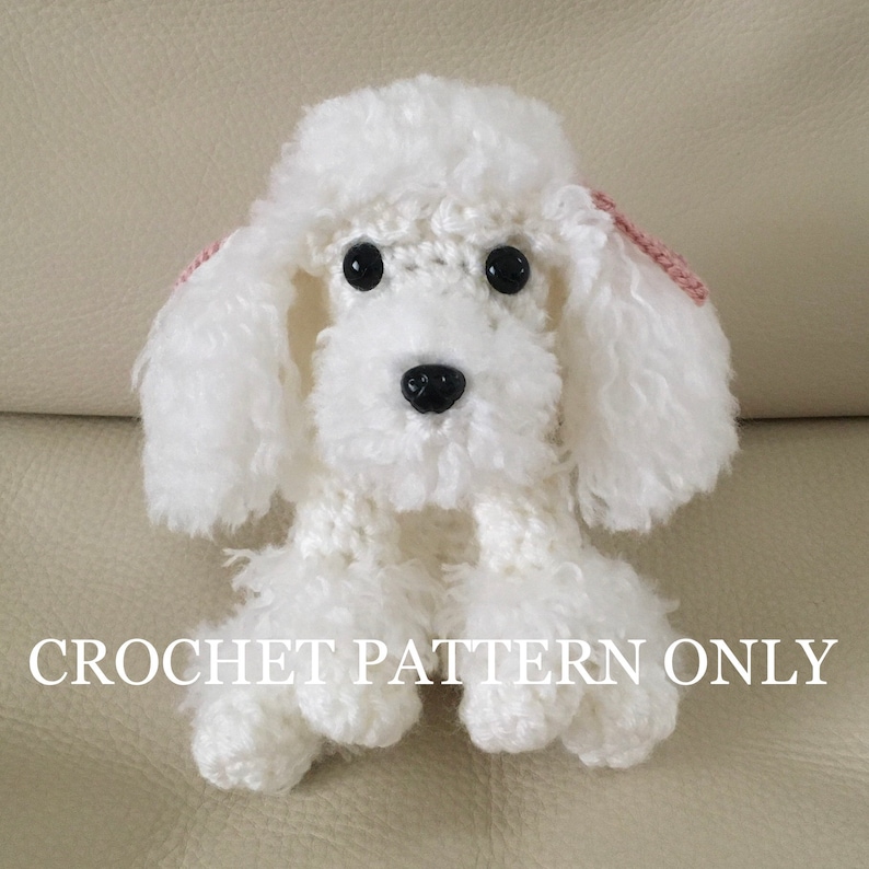 Peut inclure: Un caniche blanc en crochet avec des oreilles roses. Le caniche est assis sur une surface brun clair. CROCHET PATTERN ONLY est &eacute;crit en blanc en bas de l'image.