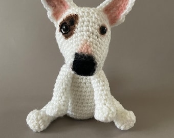May include: White crocheted stuffed bull terrier dog toy with brown and black eyes and a black nose.