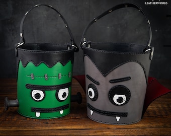 May include: Two Halloween trick-or-treat buckets made of leather. One bucket is green with a Frankenstein face and the other is grey with a vampire face.  The buckets have black leather handles and are decorated with white stitching.  DIGITAL PATTERN & VIDEO TUTORIAL