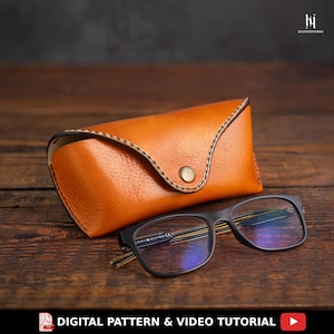 May include: A handcrafted, orange leather glasses case with a button closure, next to a pair of black-framed eyeglasses. The glasses case is stitched with a contrasting thread. The text "DIGITAL PATTERN & VIDEO TUTORIAL" is at the bottom.