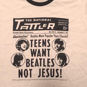 Może przedstawiać: Biała koszulka z czarnym kołnierzem z grafiką w stylu gazety. Grafika zawiera tekst "THE NATIONAL TATTLER" i "TEENS WANT BEATLES NOT JESUS!" ze zdjęciami Beatles&oacute;w.