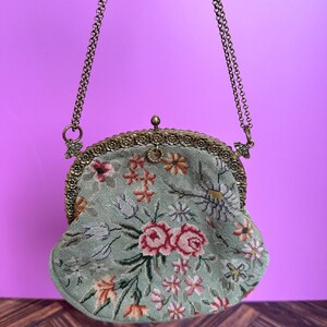 May include: A vintage floral embroidered purse with a gold chain strap and a clasp closure. The purse is green with pink, white, and yellow flowers.