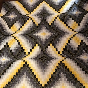 May include: A quilt with a geometric pattern of yellow and gray squares. The quilt is made of fabric with a subtle floral pattern.