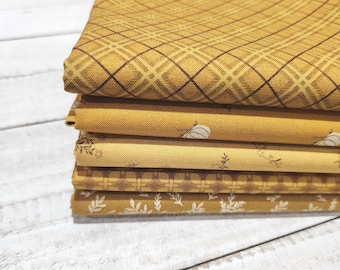 May include: A stack of five folded fabric pieces in shades of yellow and gold. The top piece features a dark brown plaid pattern, followed by a solid mustard yellow, a light yellow with small floral prints, a dark yellow grid, and a bottom piece with white leaves.