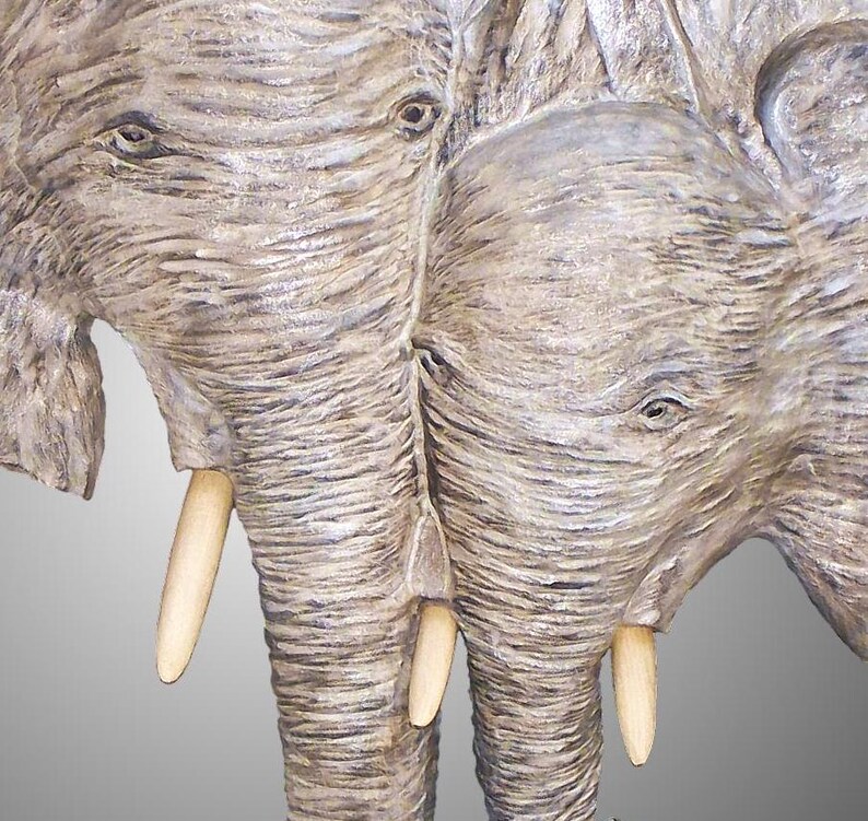 Puede incluir: Primer plano de una escultura de madera tallada de dos elefantes con colmillos de marfil. Los elefantes se miran y sus trompas se tocan.