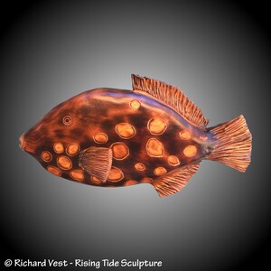 May include: A wooden sculpture of a brown and orange fish with white spots. The fish is carved in detail and has a realistic appearance.
