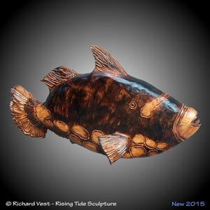 May include: A wooden sculpture of a fish with a dark brown and orange finish. The fish has a large, round body and a small, pointed head. The sculpture is detailed with scales and fins.