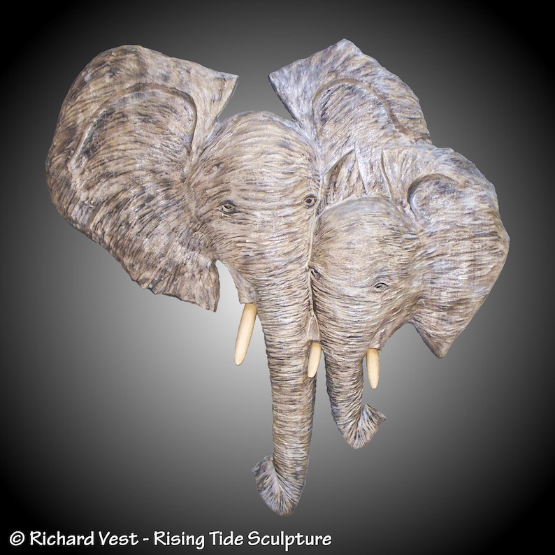 wall carving of a mother/ baby elephant front view heads and trunks.
hand carved in Alder, a brown toned wood, the artist uses a gray/white staining on each elephant and Maple, a cream toned wood, for the tusks.
for indoor display, hangers on back