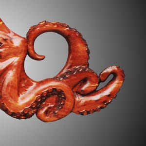Puede incluir: Primer plano de una escultura de madera de un pulpo con tent&aacute;culos detallados. La escultura est&aacute; tallada en madera de color marr&oacute;n rojizo y tiene un aspecto natural y org&aacute;nico.