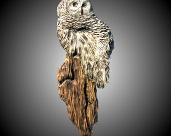 May include: A detailed wood carving of a gray owl perched on a weathered tree stump. The owl has realistic feathers and bright yellow eyes.