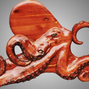 Puede incluir: Una escultura de madera de un pulpo de color marr&oacute;n rojizo. El pulpo est&aacute; tallado con detalle, con sus tent&aacute;culos y ojos claramente visibles.