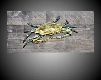 Könnte beinhalten: Eine blaue Krabben-Skulptur aus Holz, die in Gold bemalt ist und auf einem grauen Holzgrund montiert ist.