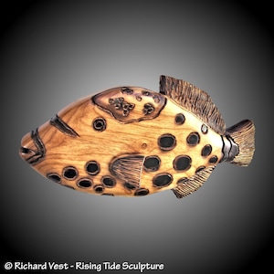 May include: A wooden sculpture of a fish with black spots and a brown and black pattern. The fish is carved in detail and has a realistic appearance.