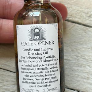 May include: A brown glass bottle with a black cap, labeled "GATE OPENER" and "SACRED WILD DIVINE." The label lists ingredients like lemongrass, citronella, and sweet almond oil. The bottle contains 1 oz of oil.
