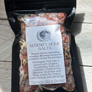 May include: A clear plastic bag filled with pink Himalayan salt crystals and dried flower petals. The bag has a label that reads "SERENITY HOME SALTS" and lists ingredients like lavender and chamomile. The text also says "SACRED WILD DIVINE".