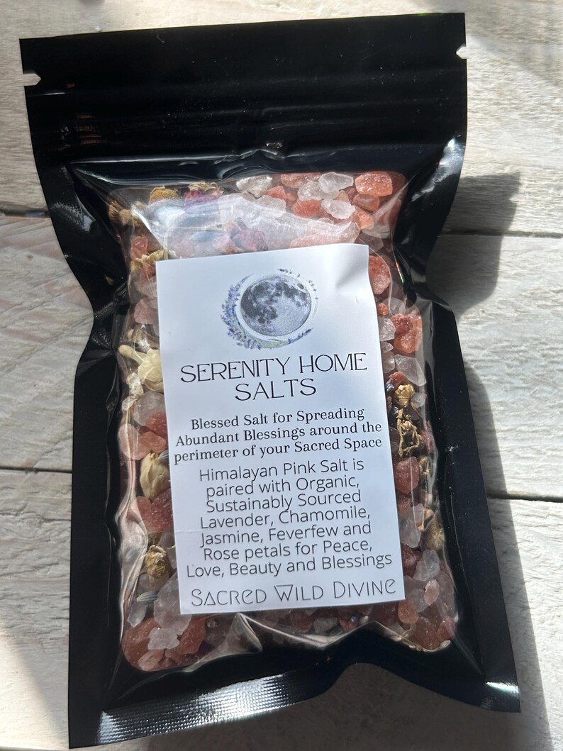 May include: A clear plastic bag filled with pink Himalayan salt crystals and dried flower petals. The bag has a label that reads "SERENITY HOME SALTS" and lists ingredients like lavender and chamomile. The text also says "SACRED WILD DIVINE".