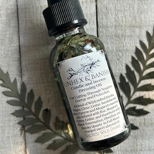May include: A clear glass bottle with a black dropper top, filled with a green liquid and herbs. The label reads "UNHEX & BANISH Candle and Incense Dressing Oil" with a list of ingredients. The bottle is 1 oz.