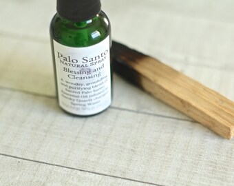Peut inclure: Une bouteille en verre vert avec une étiquette blanche qui indique "Palo Santo Natural Spray Blessing and Cleansing". Un mélange boisé, apaisant et purifiant d'huile essentielle de Palo Santo sacrée infusée de cristaux de quartz fumés et d'eau de source. Un bâtonnet de Palo Santo partiellement brûlé est posé sur une surface en bois clair.