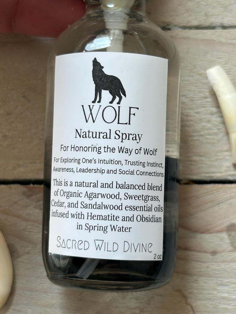 May include: A clear glass bottle with a black liquid and a white label. The label features a black silhouette of a howling wolf above the word "WOLF" and the text "Natural Spray". The bottle contains 2 oz of product.