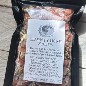 May include: A black package filled with Himalayan pink salt, lavender, chamomile, jasmine, feverfew, and rose petals. The package has a white label with the text "SERENITY HOME SALTS" and "SACRED WILD DIVINE".