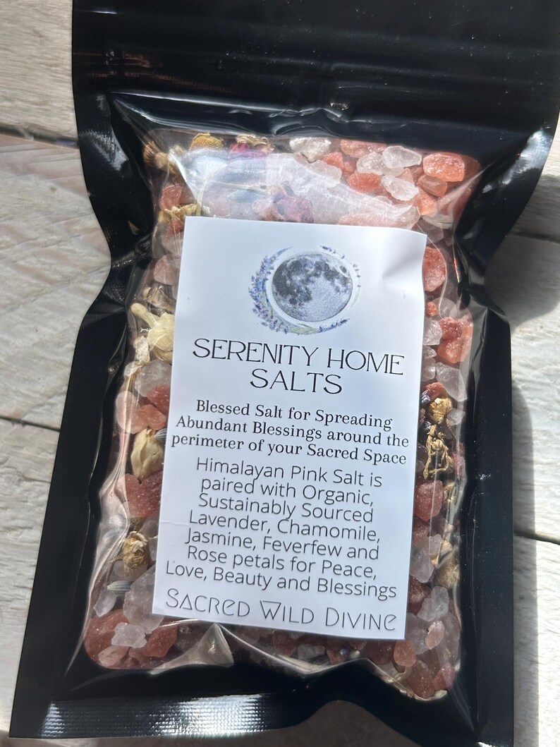 May include: A black package filled with Himalayan pink salt, lavender, chamomile, jasmine, feverfew, and rose petals. The package has a white label with the text "SERENITY HOME SALTS" and "SACRED WILD DIVINE".