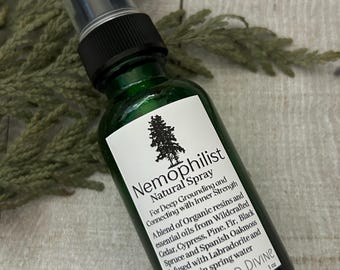 May include: A green glass bottle with a black spray top and a white label. The label reads "Nemophilist Natural Spray" and includes a description of the product's ingredients and purpose. The bottle is labeled "Sacred Wild Divine" and contains 1 oz of product.