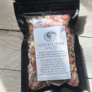 May include: A black, resealable bag filled with pink Himalayan salt and dried flower petals. A white label reads "SERENITY HOME SALTS" and lists ingredients like lavender and chamomile. The product is marketed as "Blessed Salt for Spreading Abundant Blessings."