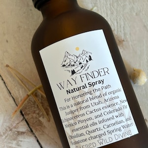 May include: A brown glass bottle with a white label that reads "WAY FINDER Natural Spray" and includes a description of the ingredients and their origins. The label also includes the text "SACRED WILD DIVINE".