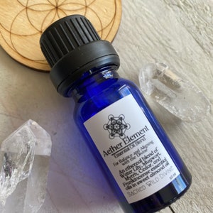 May include: A blue glass bottle with a black cap containing Aether Element Essential Oil Blend for balance and aligning with the divine. The label features a geometric design and the text "SACRED WILD DIVINE" with a 10 ml measurement.