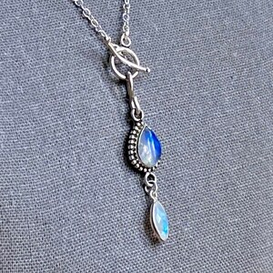 May include: A silver chain necklace with a toggle clasp and a teardrop-shaped moonstone pendant. The pendant has a smaller moonstone teardrop hanging from it.
