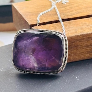 Könnte beinhalten: Eine silberne Kettenkette mit einem großen, quadratischen Amethyst-Anhänger. Der Anhänger hat einen facettierten, violetten Stein, der in einer silbernen Fassung sitzt.