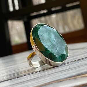 May include: A silver ring with a large, oval-shaped green gemstone. The gemstone has a faceted cut and a dark green color.