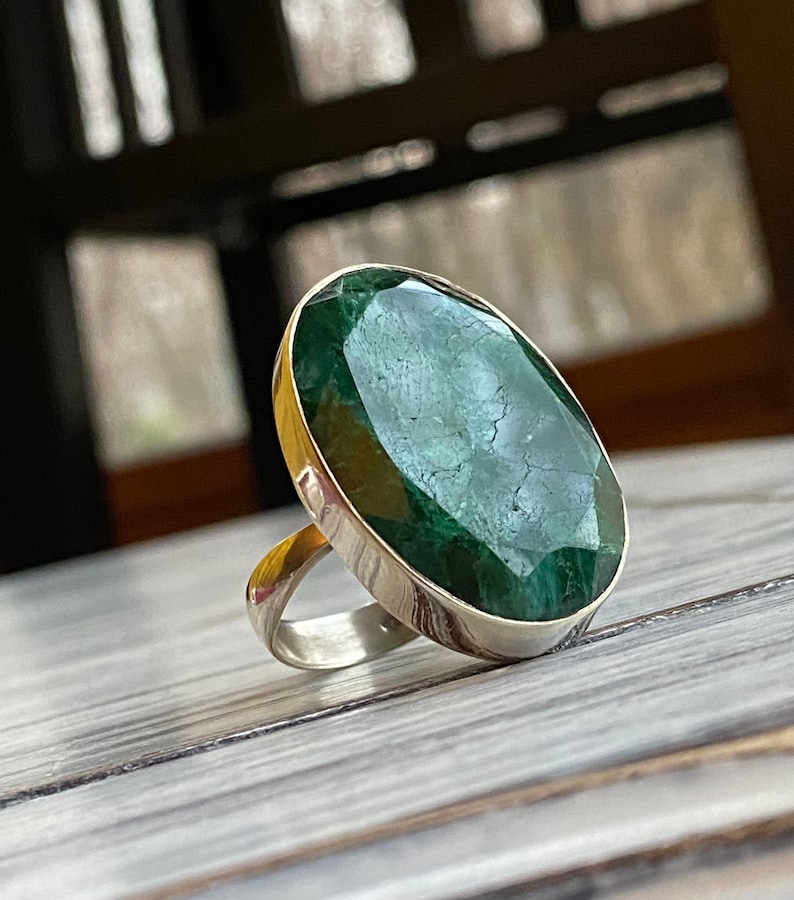 May include: A silver ring with a large, oval-shaped green gemstone. The gemstone has a faceted cut and a dark green color.