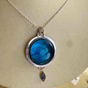 "Explore the Earth Karma Jewelry collection, showcasing Labradorite Pendants with round designs inspired by cosmic galaxies, crafted in sterling silver for a bohemian touch, and adorned with a moonstone dangle."