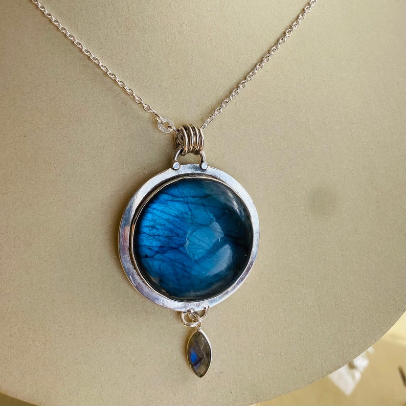 "Explore the Earth Karma Jewelry collection, showcasing Labradorite Pendants with round designs inspired by cosmic galaxies, crafted in sterling silver for a bohemian touch, and adorned with a moonstone dangle."