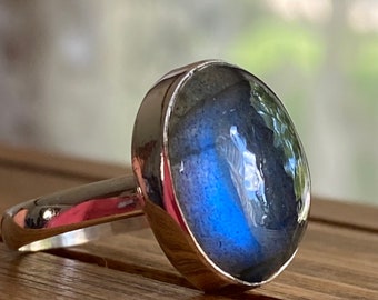 May include: A silver ring with a large oval blue labradorite gemstone. The ring is set in a simple band.