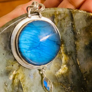 "Experience the radiant healing properties of the Earth Karma Healing Crystal Pendant, crafted in the likeness of a round cosmic galaxy, set in sterling silver, and offering timeless elegance, with an added moonstone dangle."