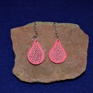 May include: A pair of pink teardrop-shaped earrings with a delicate crocheted design. The earrings are hanging from silver hooks.