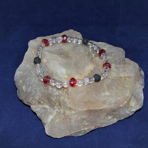 May include: A bracelet made with clear and red glass beads and black lava rock beads.
