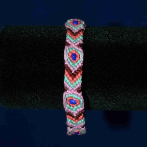 Könnte beinhalten: Ein pinkfarbenes, grünes und braunes Freundschaftsarmband mit blauen Perlen. Das Armband ist mit einem Diamantenmuster gewebt.